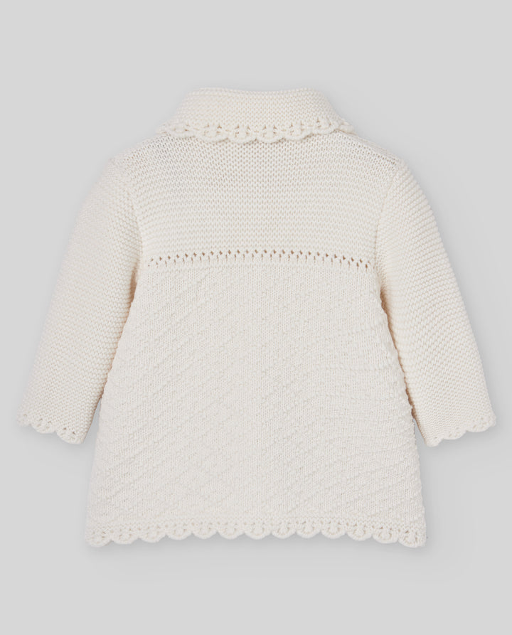 An off-white knitted baby cardigan with long sleeves, a scalloped collar, and a textured pattern on the front, shown against a neutral gray background.