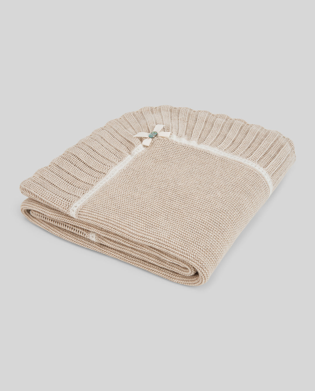 A folded beige knit blanket with a ribbed border and a small decorative bow at the corner, shown on a solid light gray background.