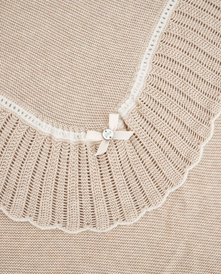 Close-up of a beige knit blanket with a wide cream lace collar and a small cream bow with a clear rhinestone at the center.