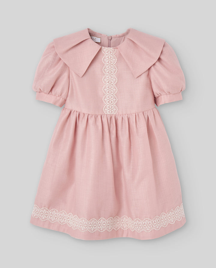 A pink short-sleeve children's dress with a large collar, gathered waist, and white lace trim on the front and hem, shown against a light gray background.