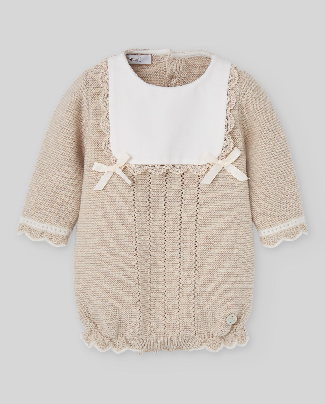 A beige knit baby romper with a contrasting white bib collar, featuring delicate lace trim, small bow details on the chest, and a ruffled hem.
