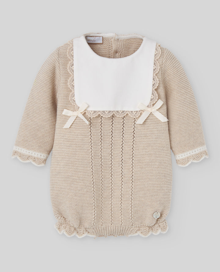 A beige knit baby romper with a contrasting white bib collar, featuring delicate lace trim, small bow details on the chest, and a ruffled hem.