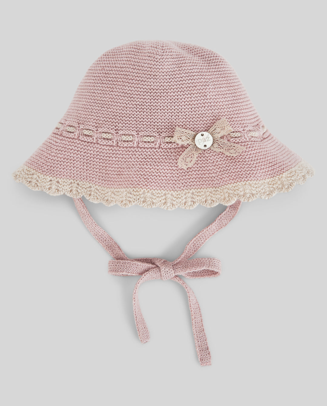Pink knitted baby hat with lace details on a light gray background