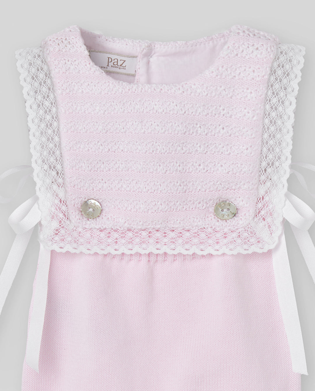 Pink romper with lace details and buttons on a light gray background