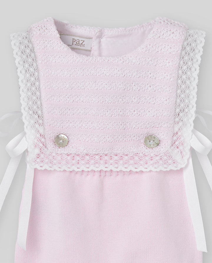 Pink romper with lace details and buttons on a light gray background