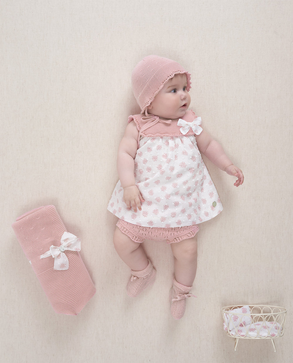 Baby in pink outfit with matching bonnet and socks on a light background