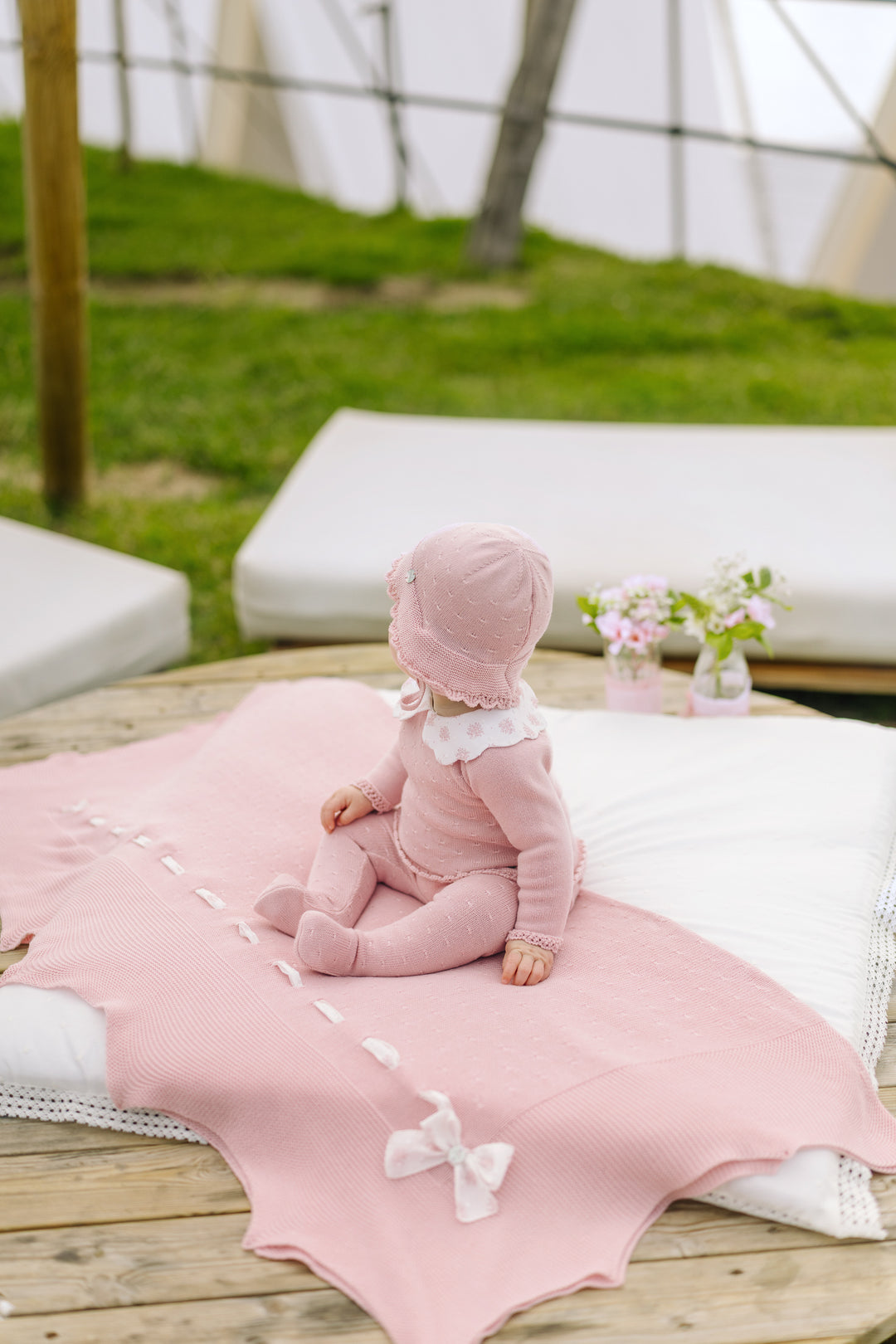 Baby in pink outfit sitting on a pink blanket outdoors