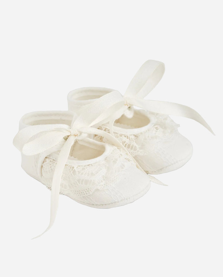 Pair of white baby shoes with lace details on a white background