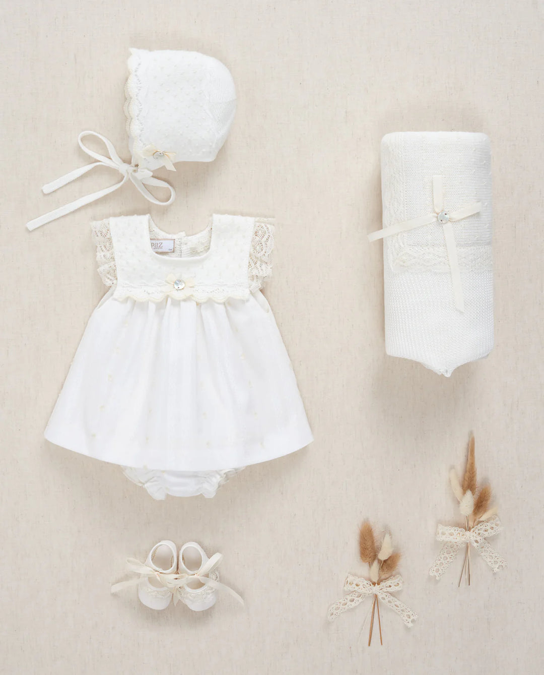Baby girl special occasion dress next to a baby bonnet and blanket