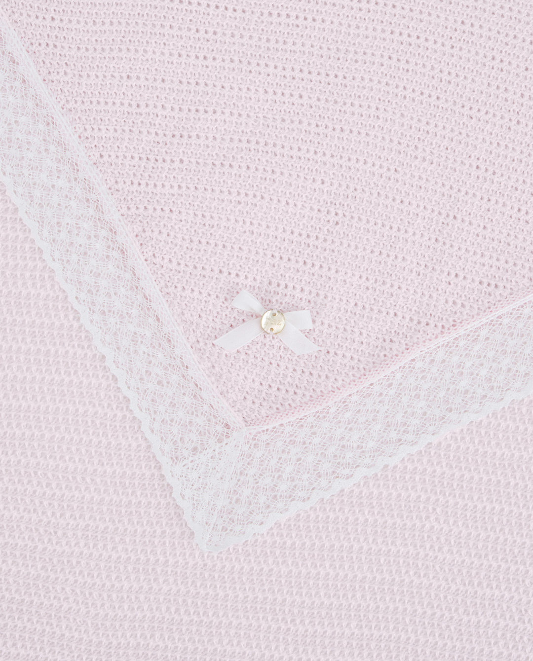 Close-up of a light pink knitted blanket with a pearl button detail.
