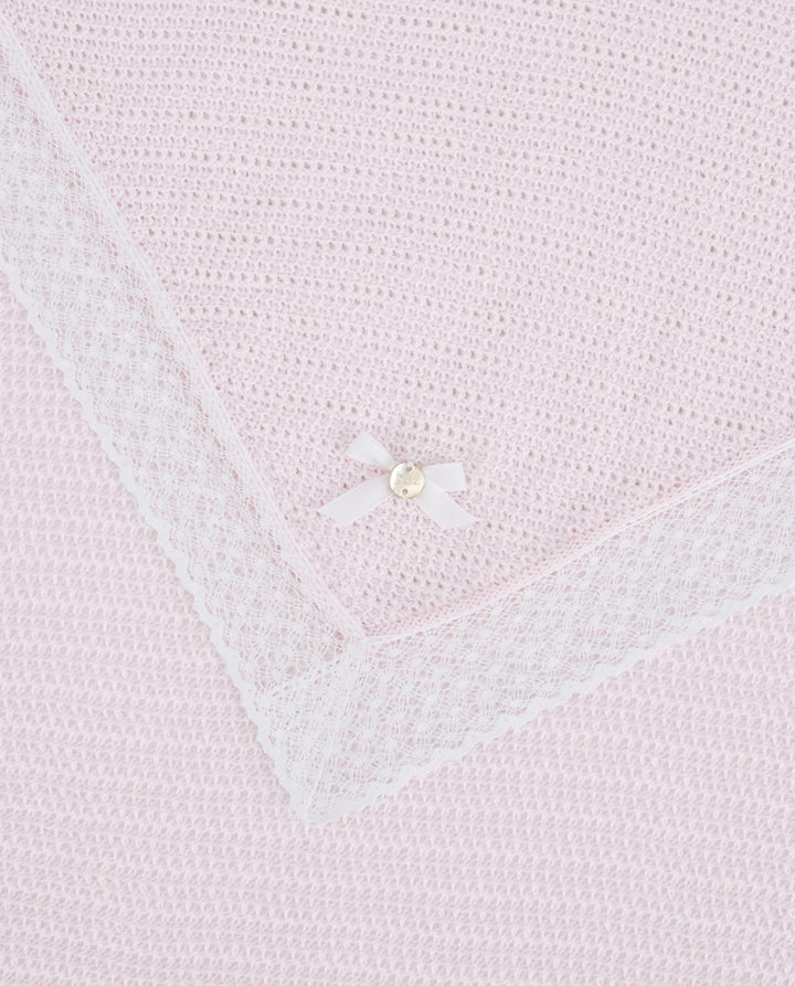 Close-up of a light pink knitted blanket with a pearl button detail.