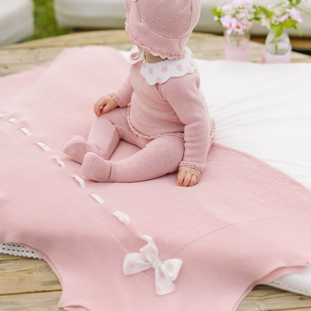 Baby in pink outfit sitting on a pink blanket outdoors
