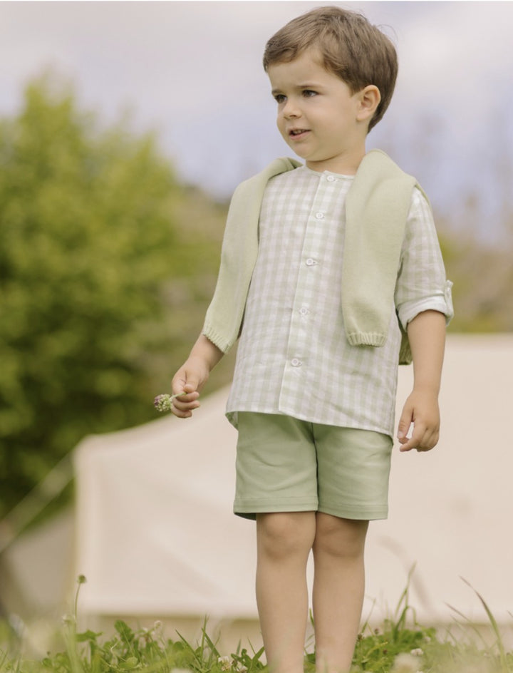 Young boy in a light green outfit standing outdoors with a blurred background