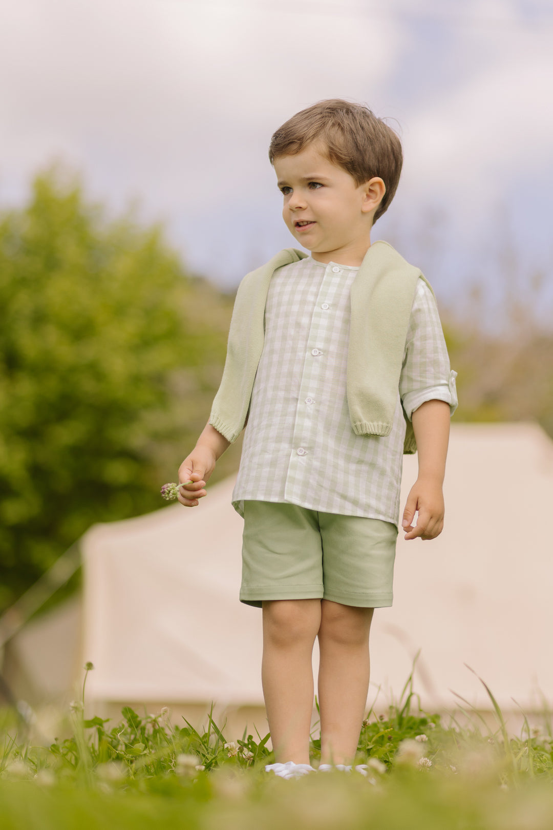 Young boy in a light green outfit standing outdoors with a blurred background