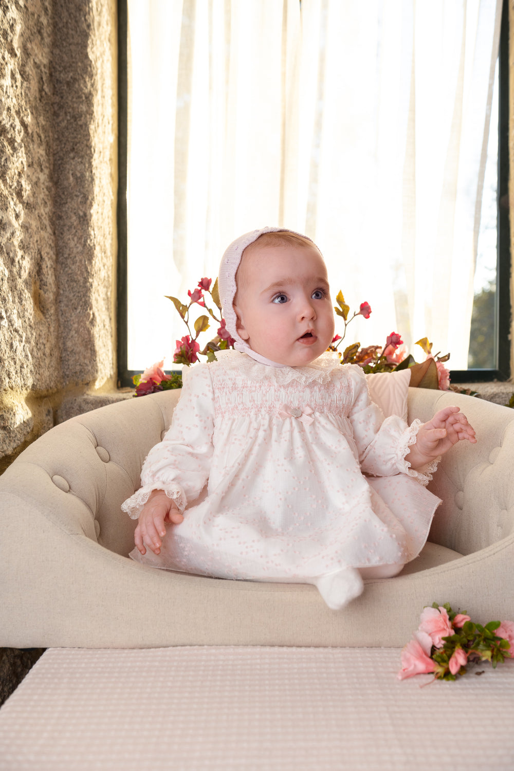 baby girl sitting in a chair wearing a white smocked dress with pink details