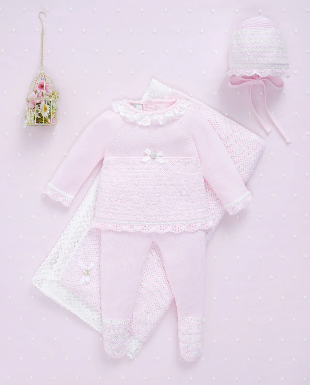 Baby outfit set with pink long-sleeve top, pants, and hat on a light pink background.