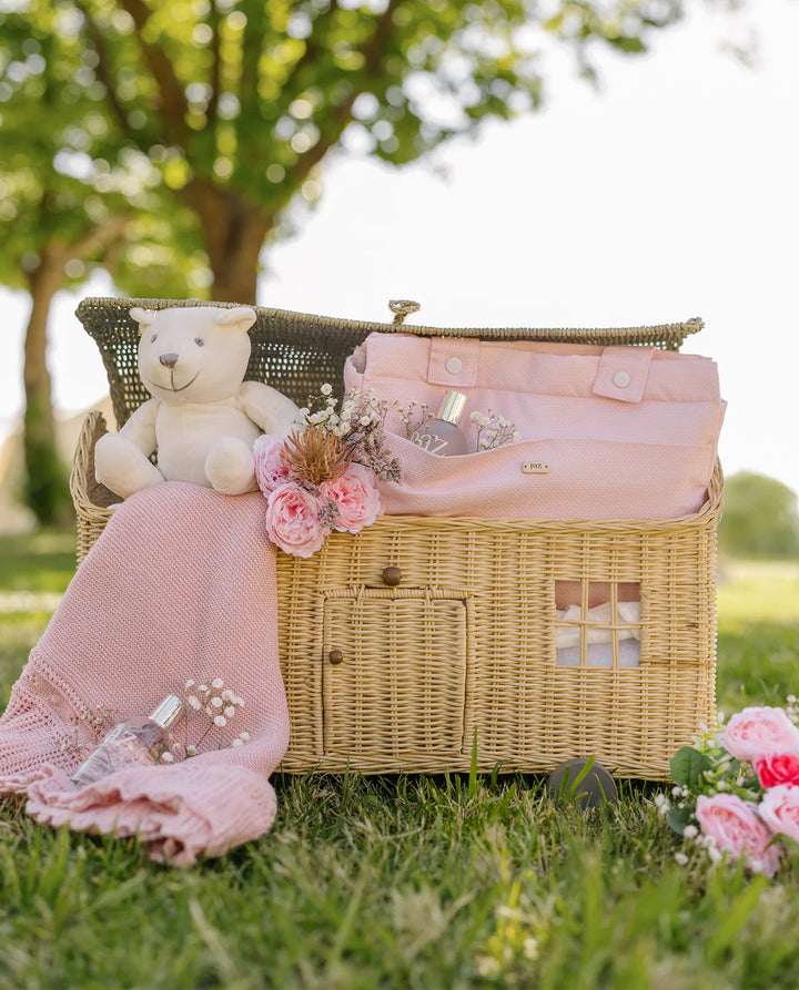 Wicker picnic basket with pink blanket, teddy bear, and flowers on grass