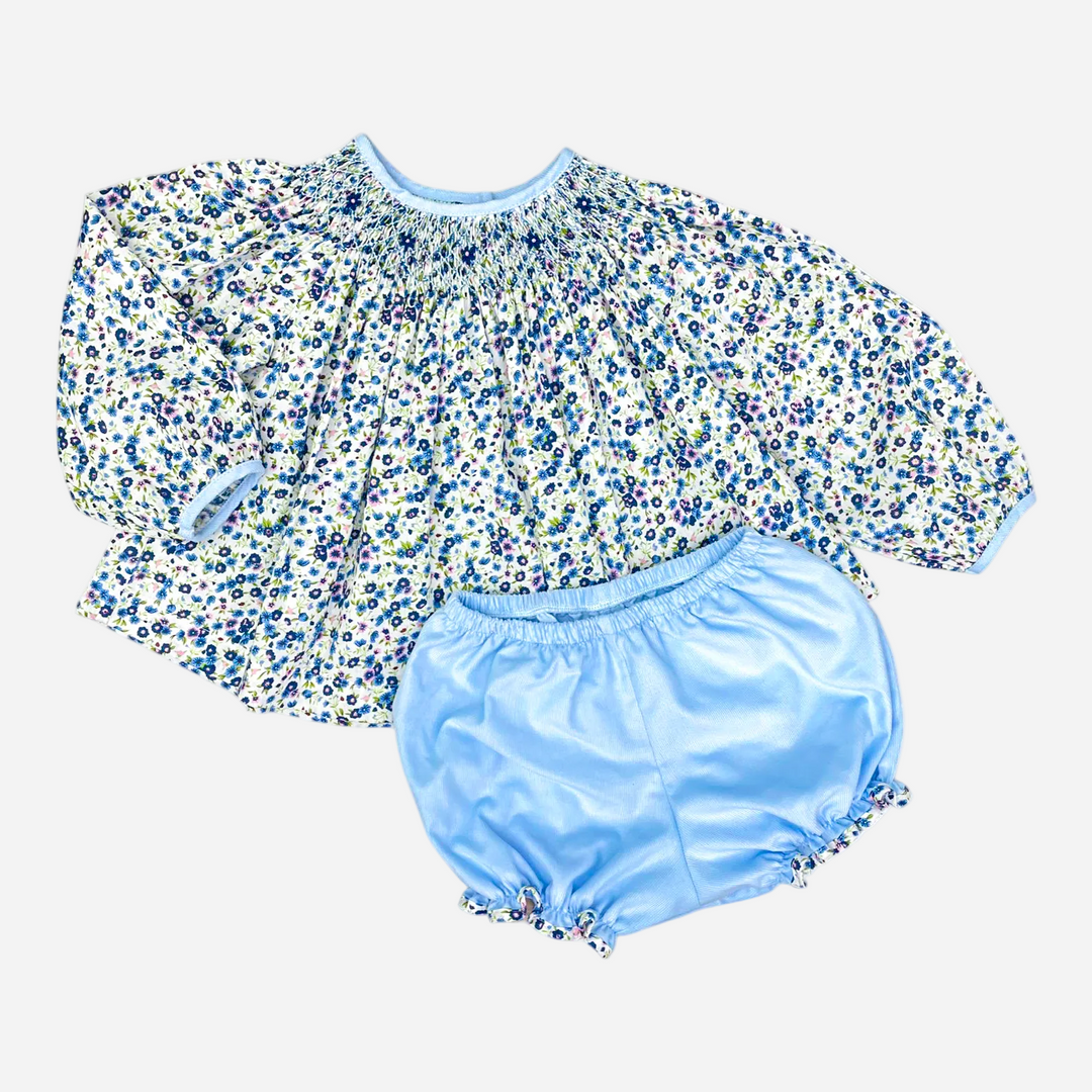 A two-piece baby outfit set featuring a long-sleeve smocked blouse with a blue, green, and white floral print, paired with light blue satin bloomers, shown on a plain white background.
