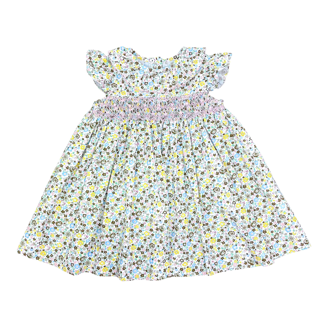 A baby girl's dress with a white background, a dense yellow, blue, and gray floral print, ruffled cap sleeves, and a smocked waistband.