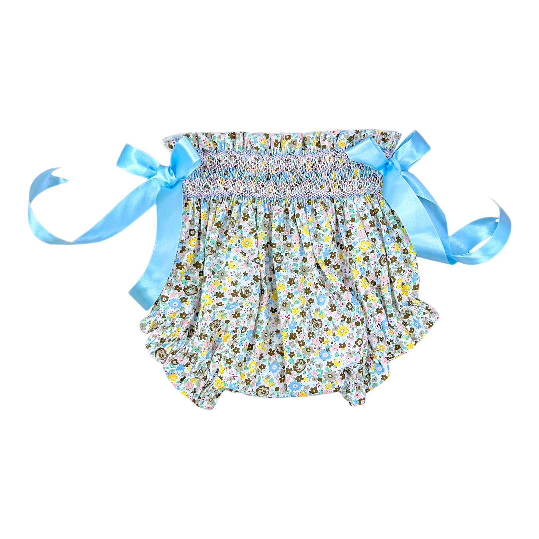 A baby girl's smocked ruffle bloomers featuring a multicolor floral print on a white background with light blue satin side ribbons tied into bows.
