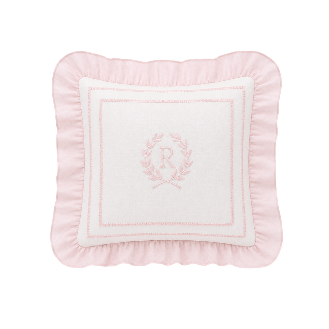 A square decorative throw pillow in light pink with a white center panel featuring a pink embroidered monogram wreath and border, set against a plain white background.