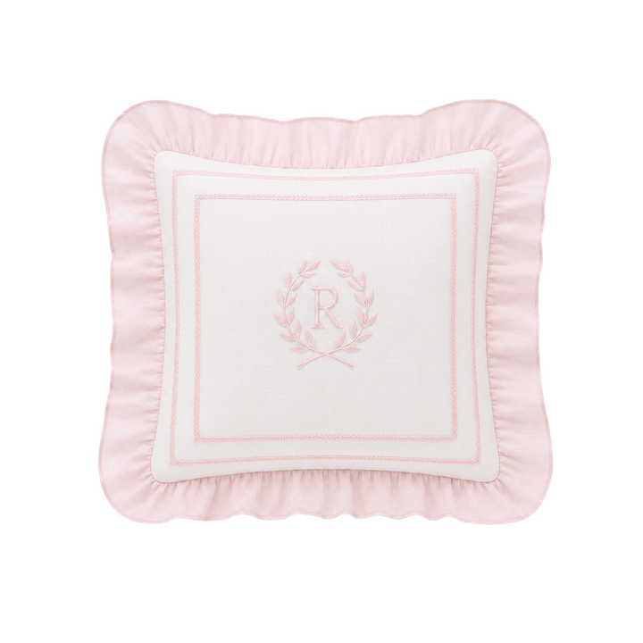 A square decorative throw pillow in light pink with a white center panel featuring a pink embroidered monogram wreath and border, set against a plain white background.