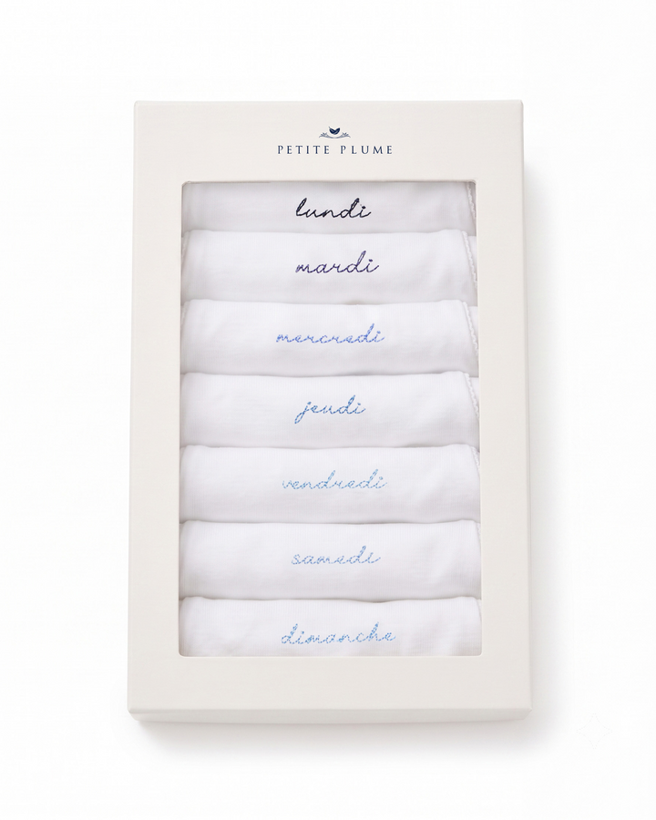 A boxed set of six folded white fabric items, likely baby cloths or swaddle blankets, arranged in a clear-front cream box. The top of the box is printed with the brand name 'Petite Flôme' and each folded piece is labeled with the day of the week in French in blue script.