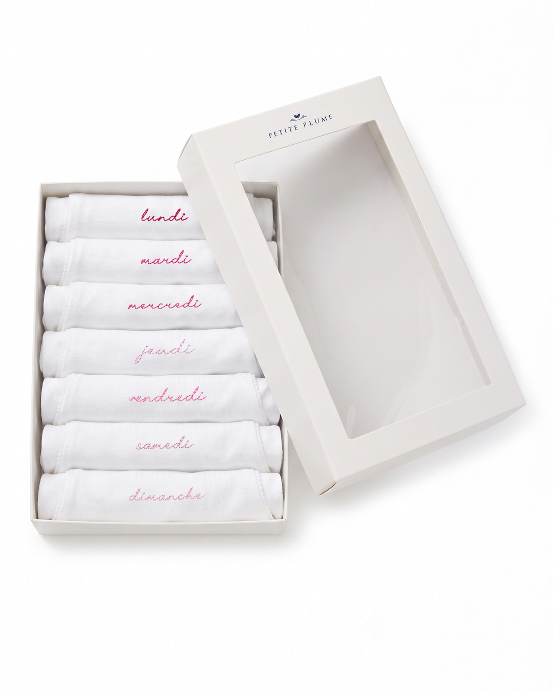 A boxed set of six folded white baby socks or handkerchiefs in a white presentation box with a clear window, shown on a white background. The folded pieces are labeled in pink script with the days of the week in Italian: lunedì, martedì, mercoledì, giovedì, venerdì, sabato, e domenica.