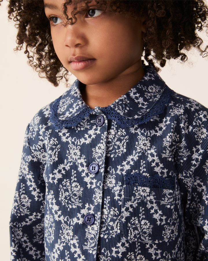 A close-up of a young girl wearing a navy blue and white floral corduroy shirt with a lace Peter Pan collar and matching buttons.