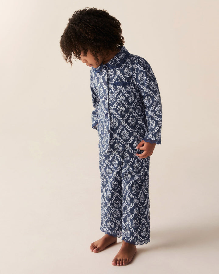 A child wearing a navy blue and white patterned long-sleeve pajama set, standing barefoot against a plain beige studio background.