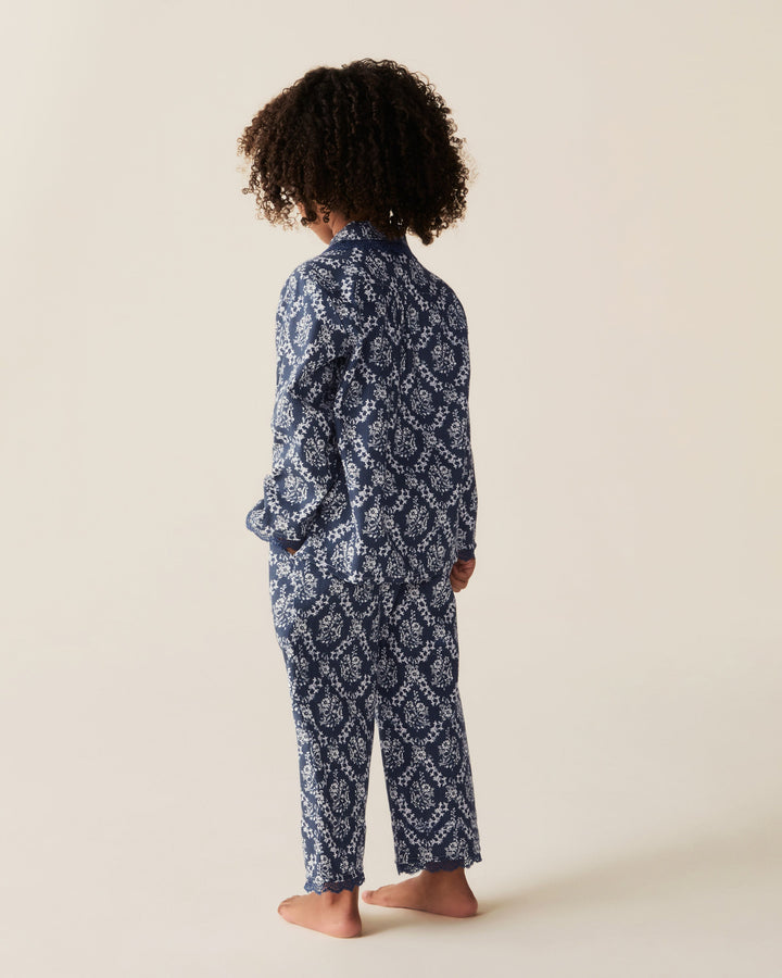 A child standing barefoot from the back, wearing a navy and white patterned long-sleeve pajama set against a plain beige studio background.