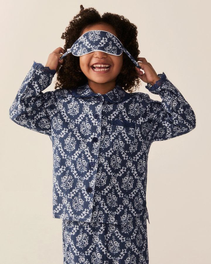 A smiling child wearing a matching long-sleeve pajama set and sleep mask, featuring a navy blue and white floral pattern, against a solid light beige background.