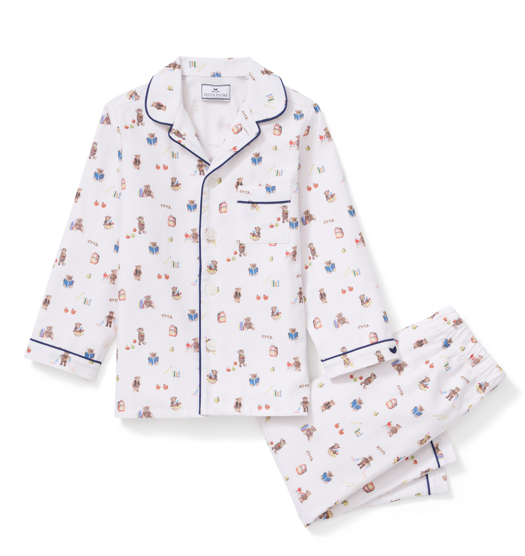 A two-piece pajama set featuring a long-sleeve button-front top and matching pants. The pajamas are white with a small, all-over teddy bear pattern in muted red, blue, and brown, and are finished with dark blue piping along the collar, cuffs, and front placket.