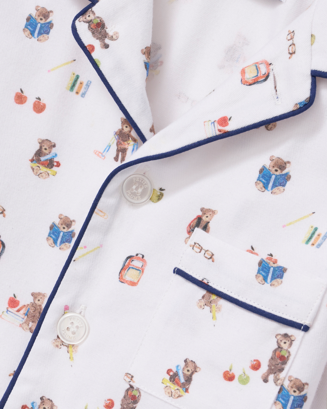 Close-up of a white pajama shirt with a playful teddy bear school-themed print and navy blue piping trim.