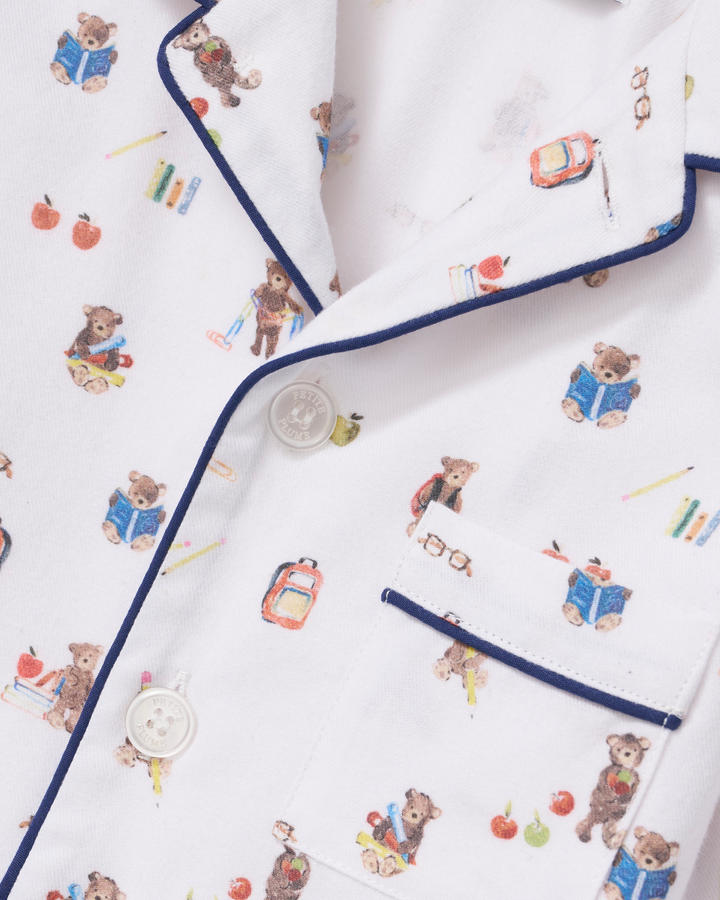 Close-up of a white pajama shirt with a playful teddy bear school-themed print and navy blue piping trim.