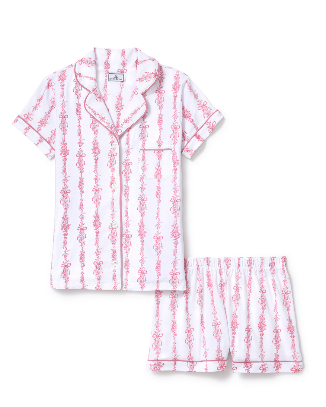 A two-piece women's pajama set featuring a short-sleeve button-front top and matching shorts, both in white with a vertical pink pattern of stylized figures and piping trim.