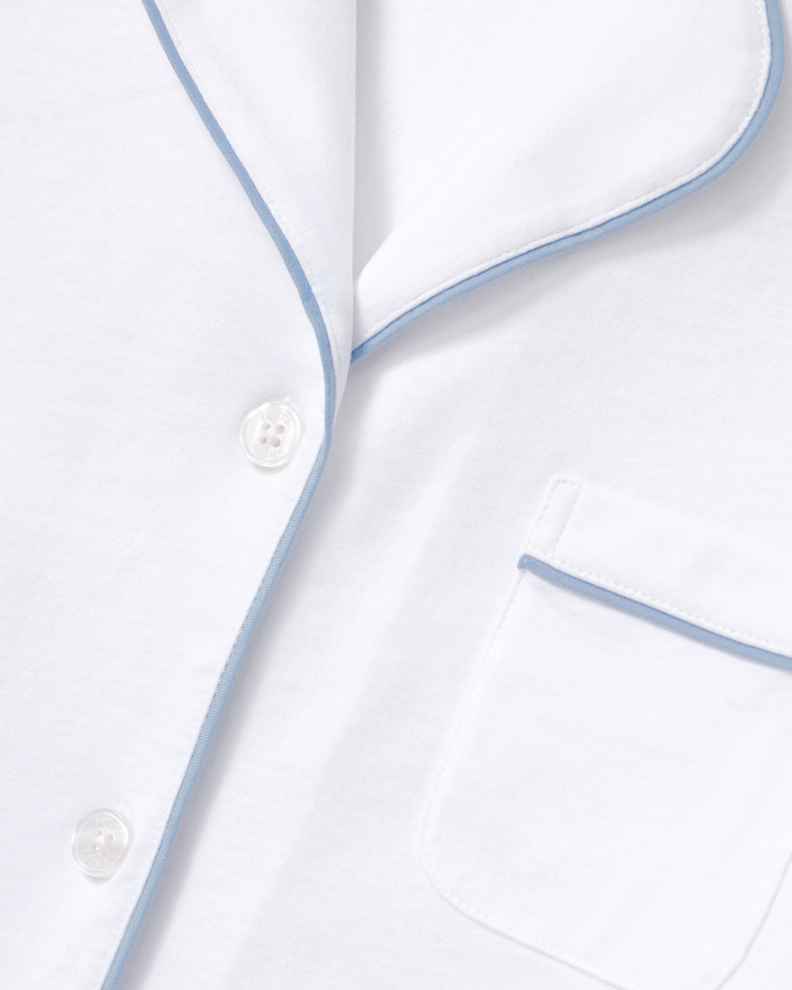Close-up of a white pajama shirt with light blue piping trim and white buttons, showing part of the collar and a chest pocket.