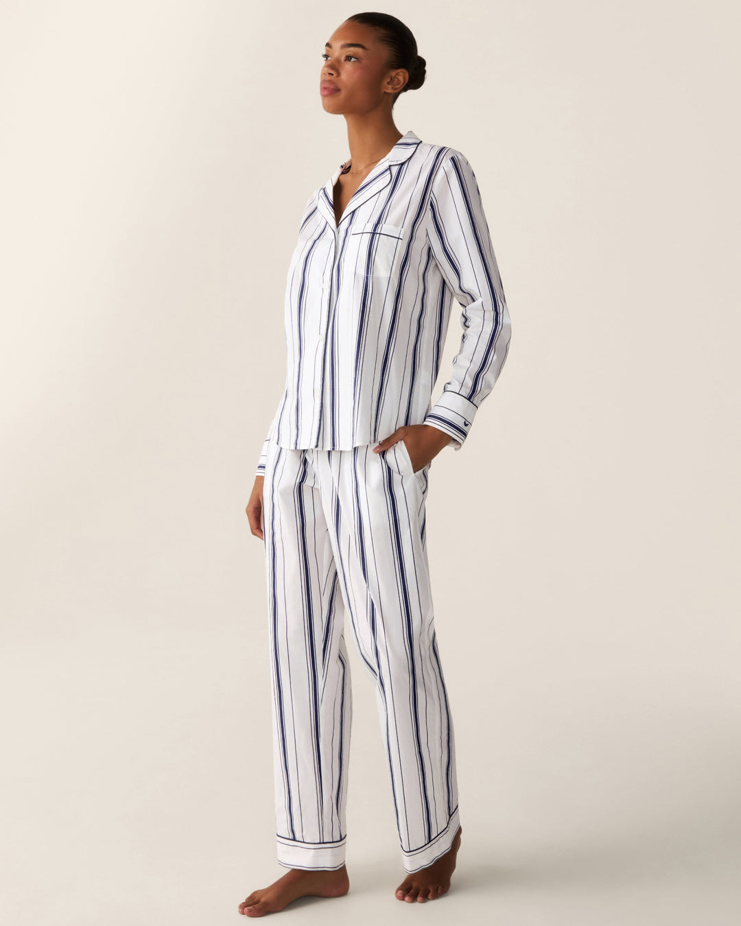 A woman modeling a matching long-sleeve pajama set with vertical navy blue stripes on a white background, photographed against a plain light beige studio backdrop.