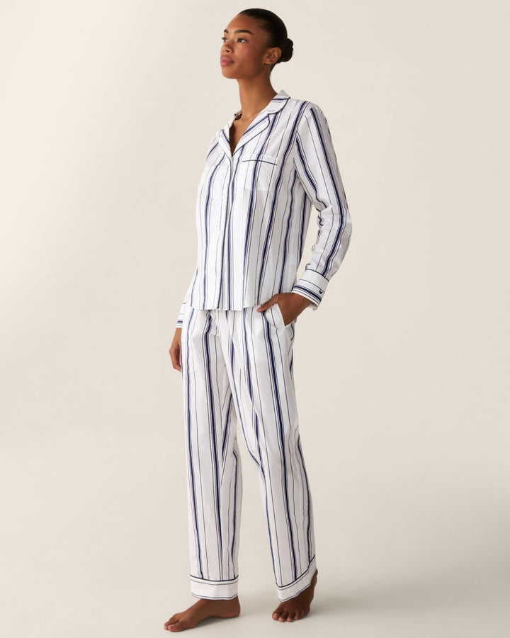A woman modeling a matching long-sleeve pajama set with vertical navy blue stripes on a white background, photographed against a plain light beige studio backdrop.
