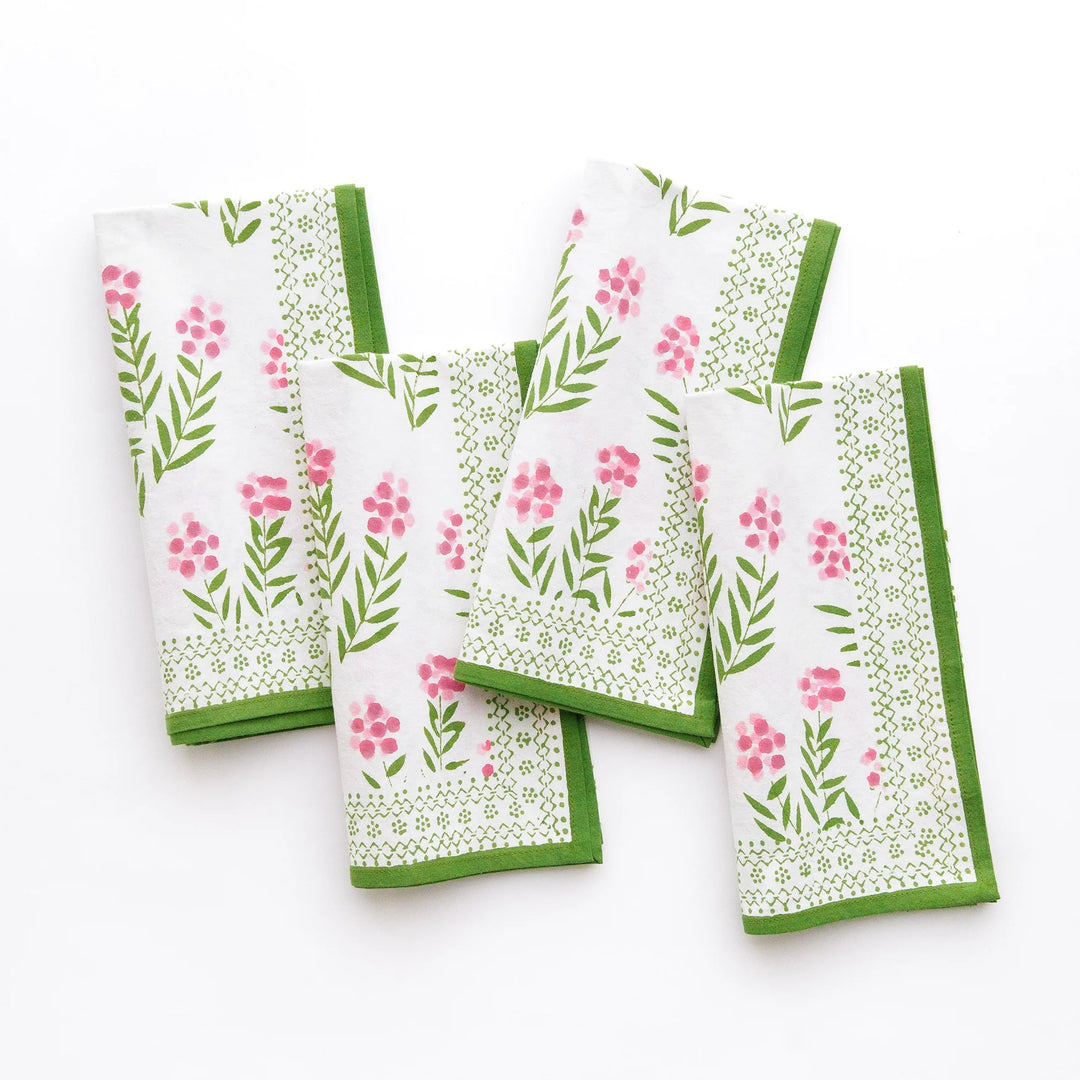 Set of four floral patterned napkins with green borders on a white background