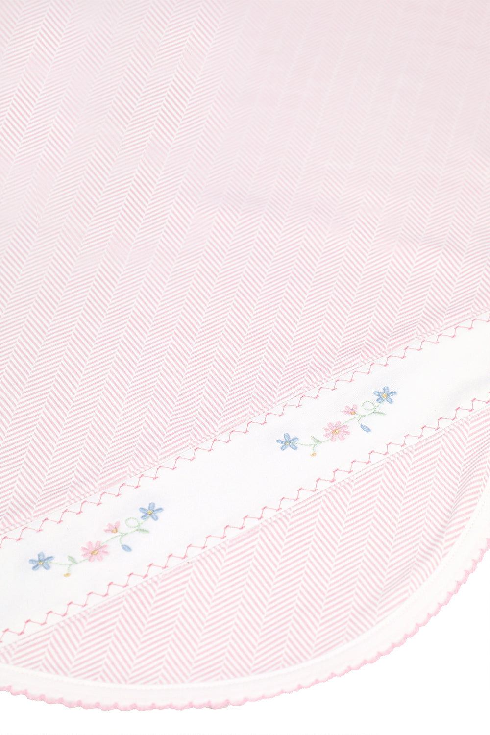 A close-up of a light pink herringbone-patterned fabric with a white border featuring delicate embroidered flowers and scalloped edges.