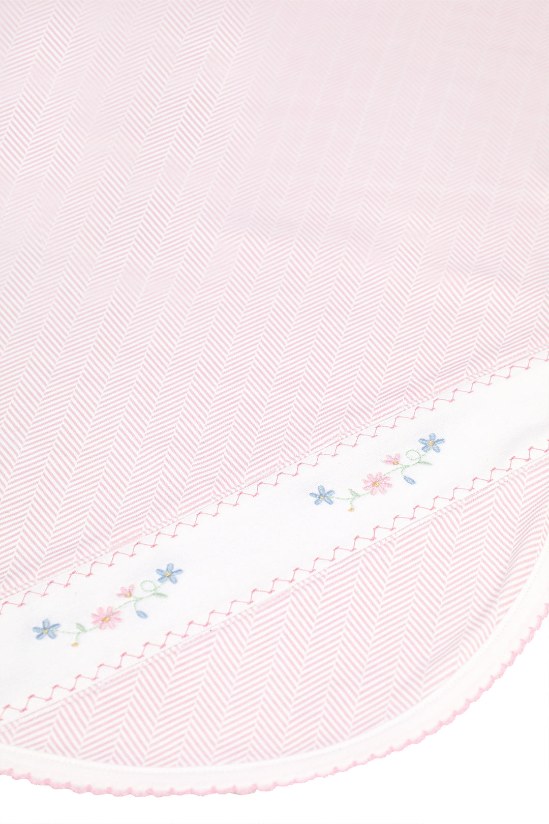 A close-up of a light pink herringbone-patterned fabric with a white border featuring delicate embroidered flowers and scalloped edges.