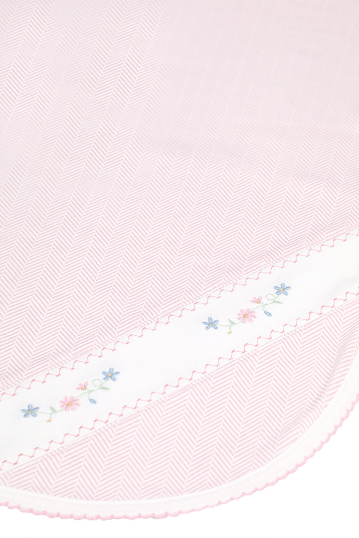 A close-up of a light pink herringbone-patterned fabric with a white border featuring delicate embroidered flowers and scalloped edges.
