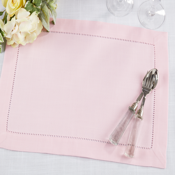 Silver cutlery with decorative handles on a pink placemat with flowers and glasses in the background.