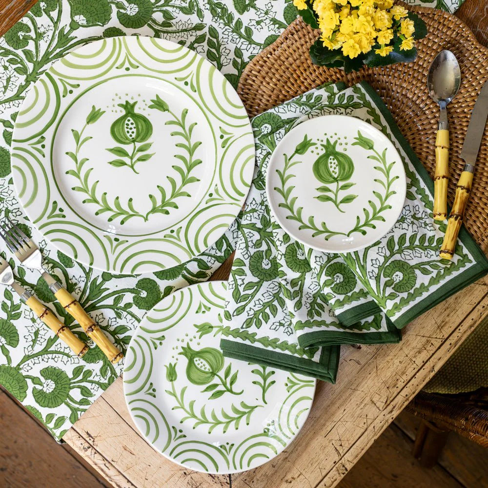 Dining table setting with green and white patterned plates, napkins, and cutlery.