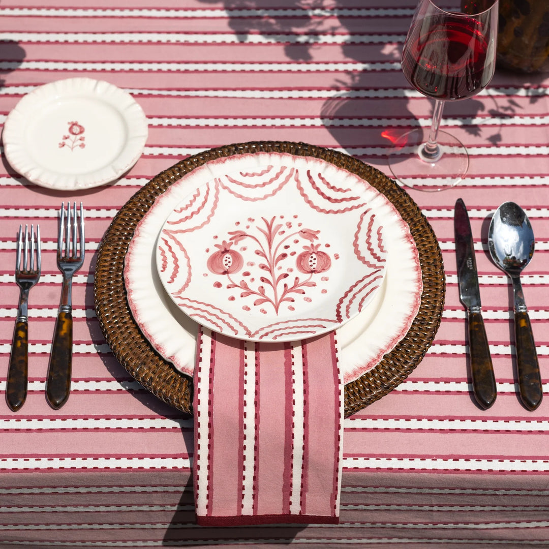 Dining table setting with patterned plates, cutlery, and a striped tablecloth.