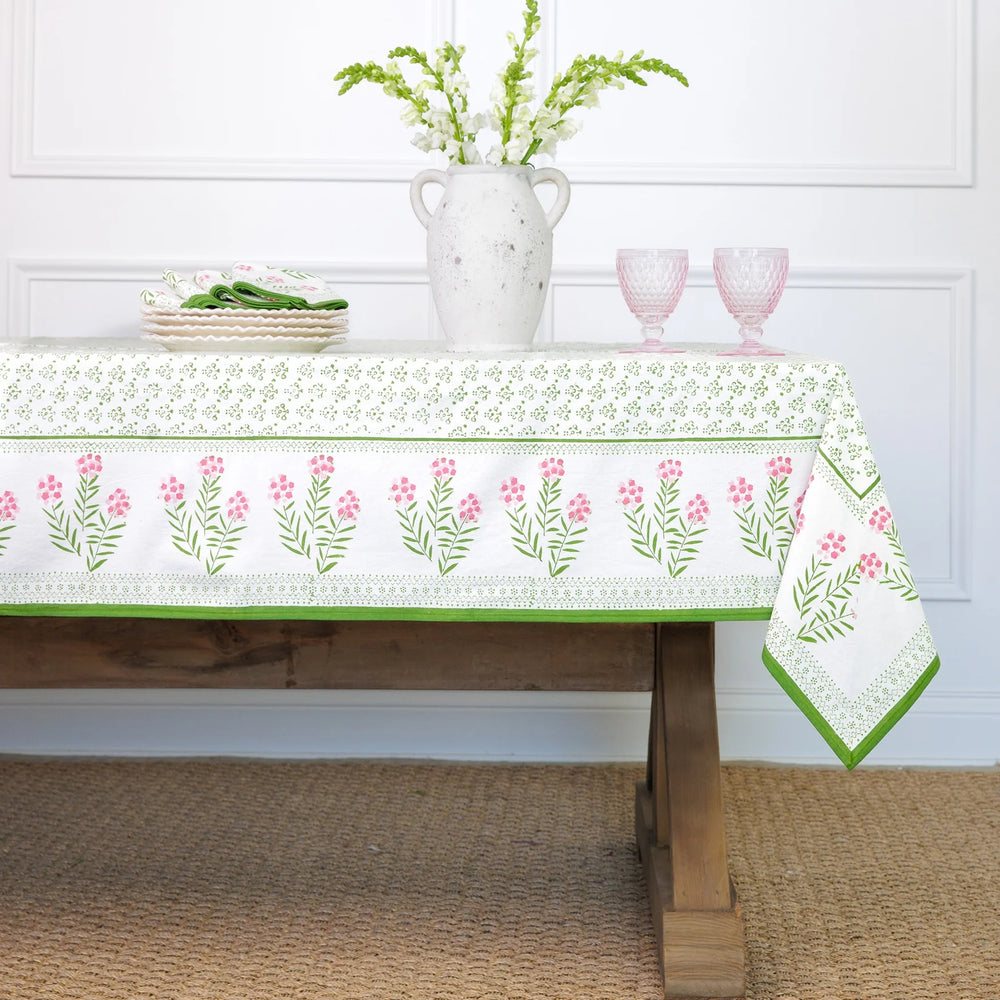 Tablecloth with floral pattern on a wooden table against a white paneled wall.