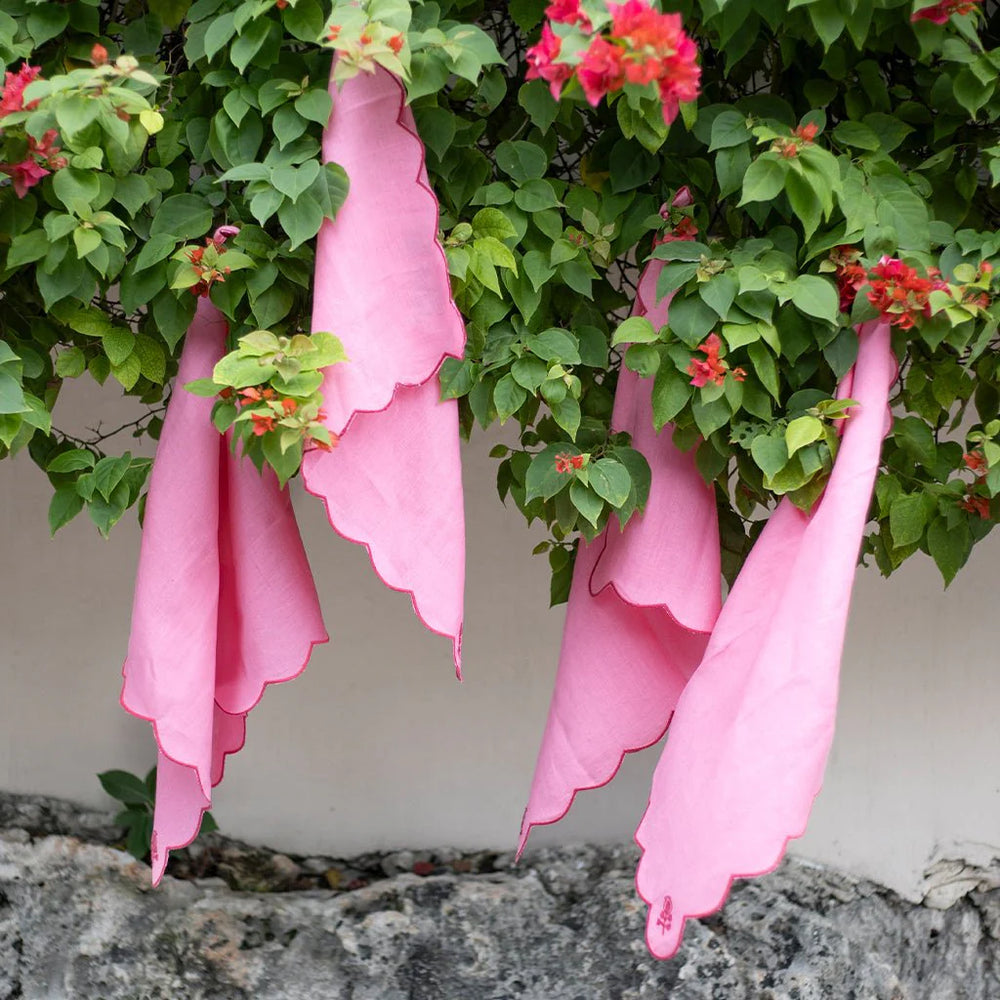 Pink dinner napkins hanging among green foliage and red flowers.