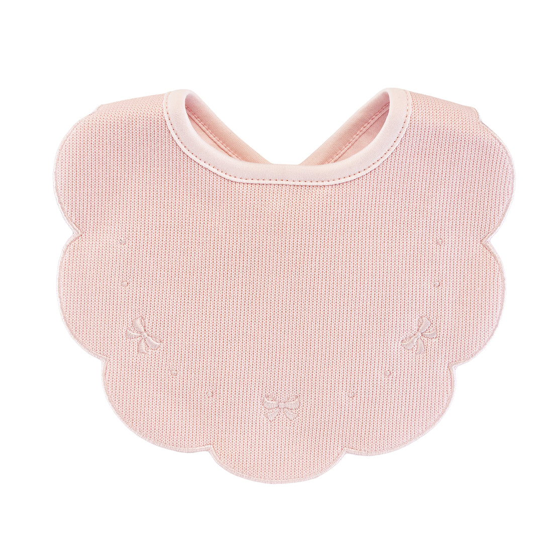 A light pink textured baby bib with a scalloped edge and small embroidered bow details, shown on a plain white background.