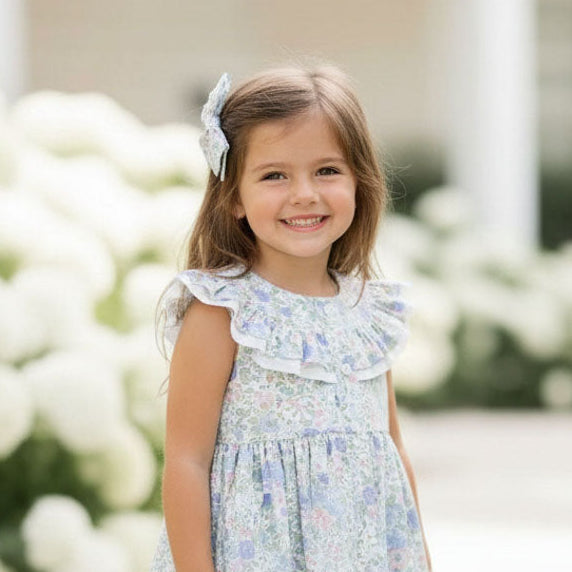 Young girl in a floral dress standing on a stone path with white flowers in the background